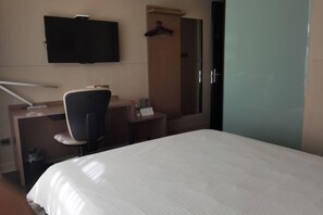 Una habitación de hotel con cama, escritorio con silla, televisión y armario.