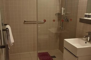 Un baño con cabina de ducha de vidrio, un lavabo blanco y un perchero para toallas.