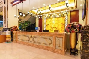 A hotel reception area with a marble counter, a reception desk, a large vase of flowers, and a staircase in the background. - Textile City Hotel (Nantong)