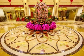 Un hall d’entrée agrémenté d’une composition florale centrale, d’un sol orné de motifs circulaires et, au fond, d’un imposant escalier.