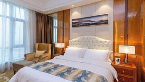 Habitación de hotel con una cama grande, una silla, una mesita de noche con lámparas, un cuadro en la pared y vistas al exterior.