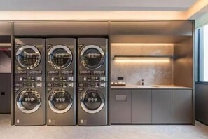 A modern laundry facility with three stacked washing machines and a countertop with a sink. - Textile City Hotel (Nantong)