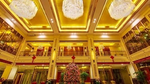 Un lobby de hotel imponente con varios pisos, grandes candelabros y un arreglo floral central.