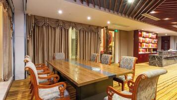 A conference room with a long table and chairs, a patterned carpet, and a bookshelf in the background.