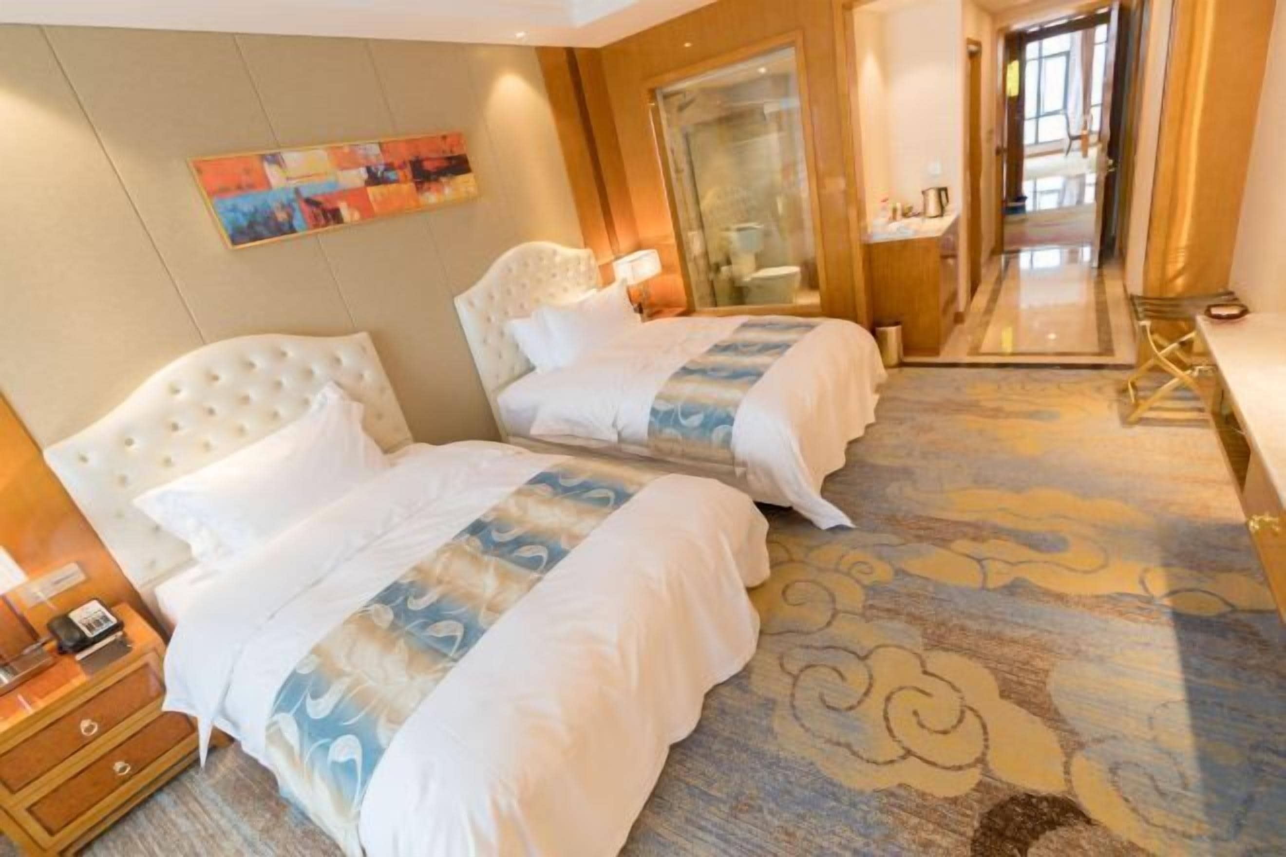 Habitación de hotel con dos camas, un espejo grande, un cuadro en la pared y una alfombra con estampado de nubes.