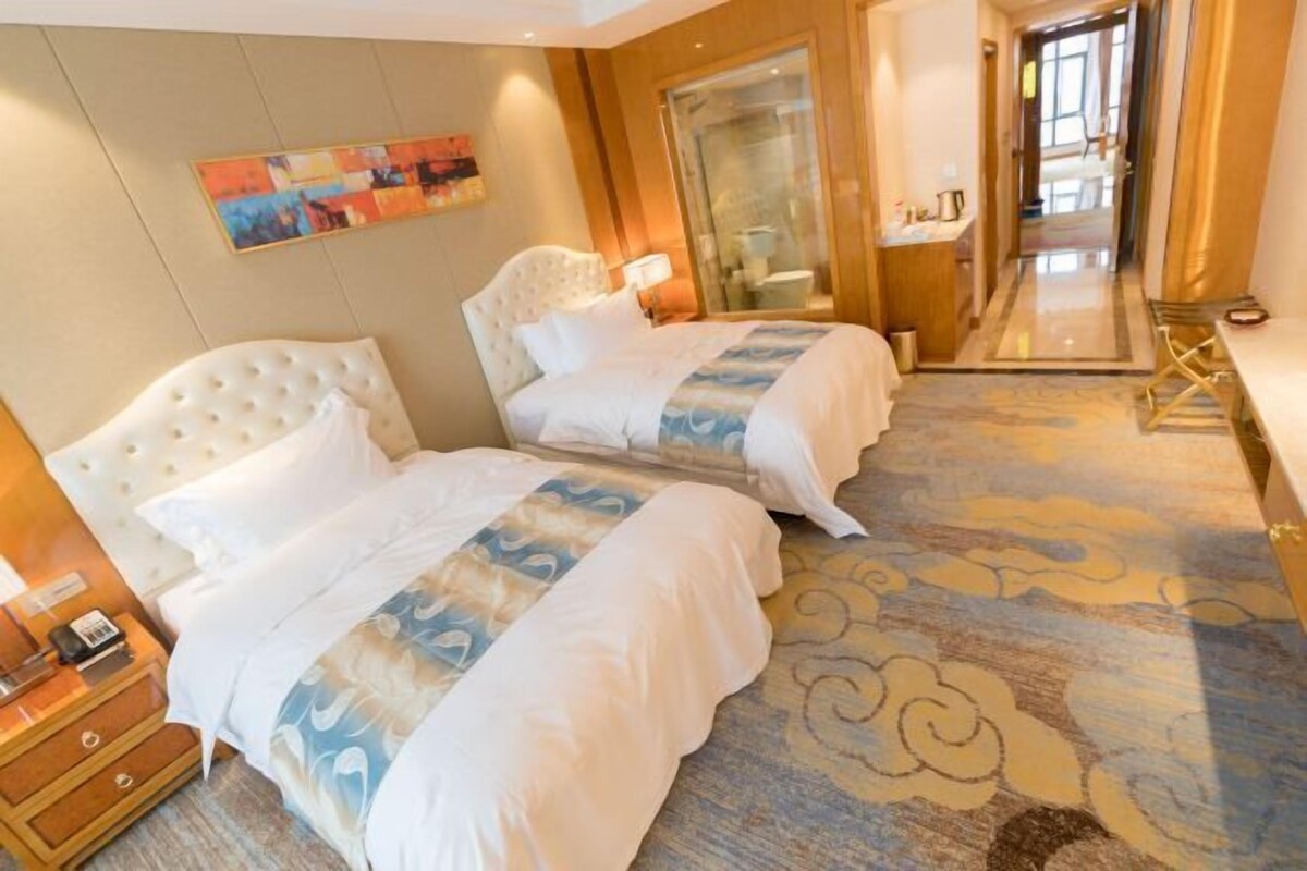 A hotel room with two beds, a large mirror, a painting on the wall, and a carpet with a cloud pattern.