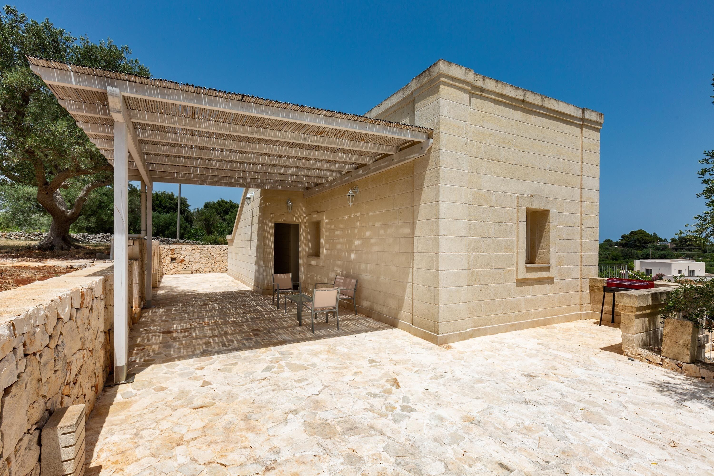 A stone building with a tiled patio, outdoor seating, and a pergola.