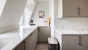Eine moderne Küche mit weißen Marmorarbeitsplatten, einer kleinen Mülltonne und einem gerahmten Bild an der Wand.