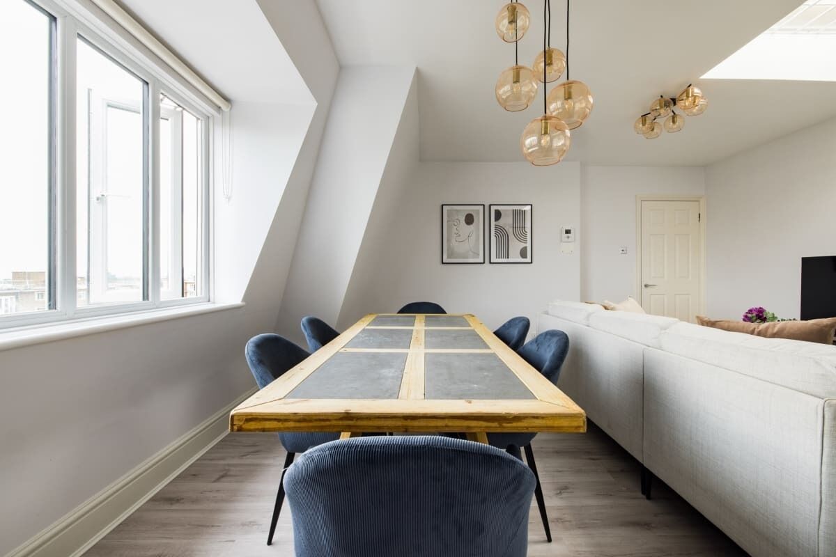 A modern living room with a dining table, chairs, a sofa, and a ceiling light fixture.