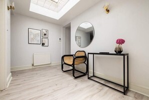 Una habitación moderna con tragaluz, un espejo redondo, una consola con un florero y dos sillas.