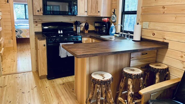 Une cuisine rustique, aménagée dans une cabane en bois, avec un îlot central, des tabourets de bar, une cuisinière et un four à micro-ondes.