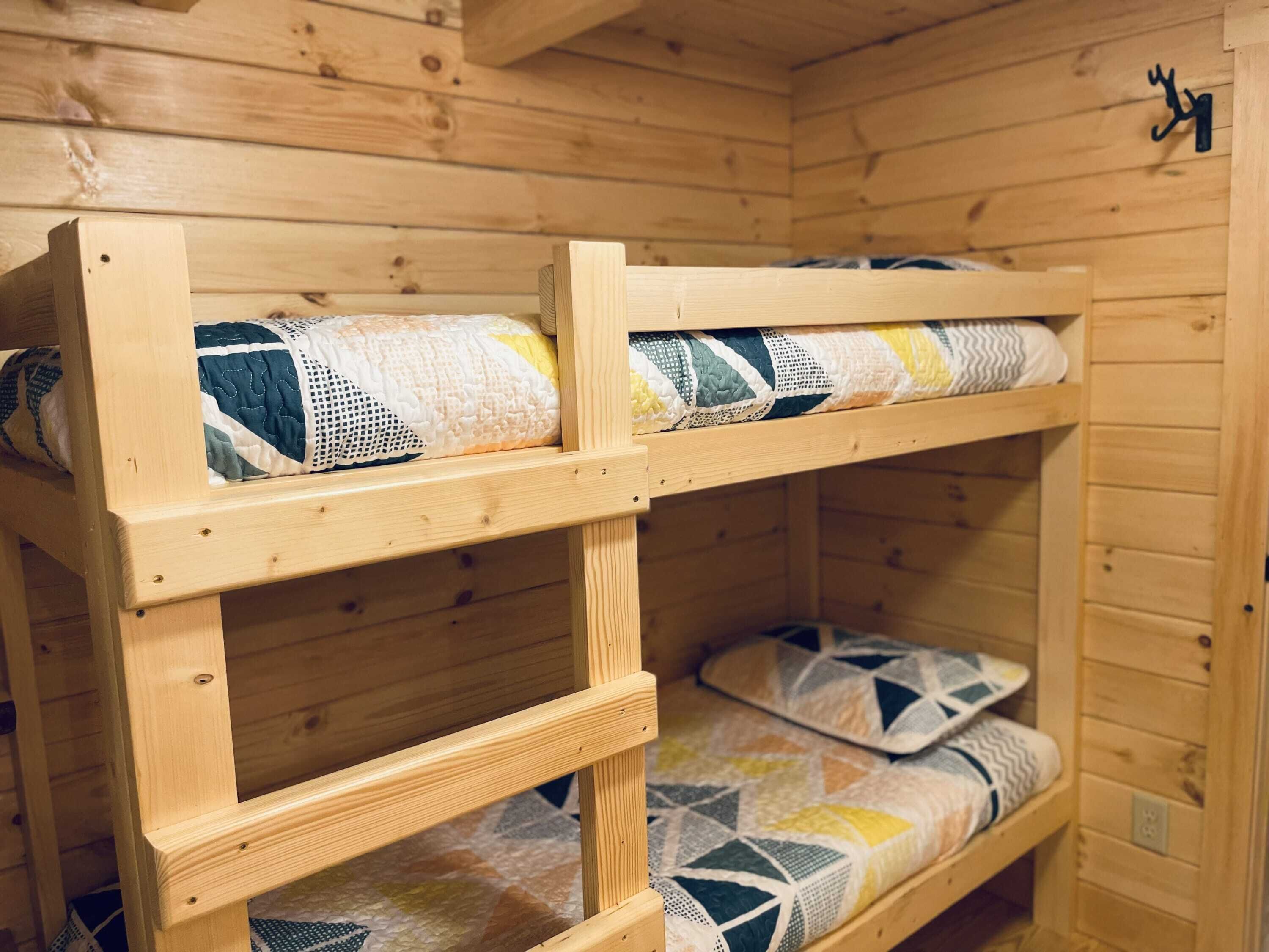 A wooden bunk bed with two levels, each with a quilted mattress.