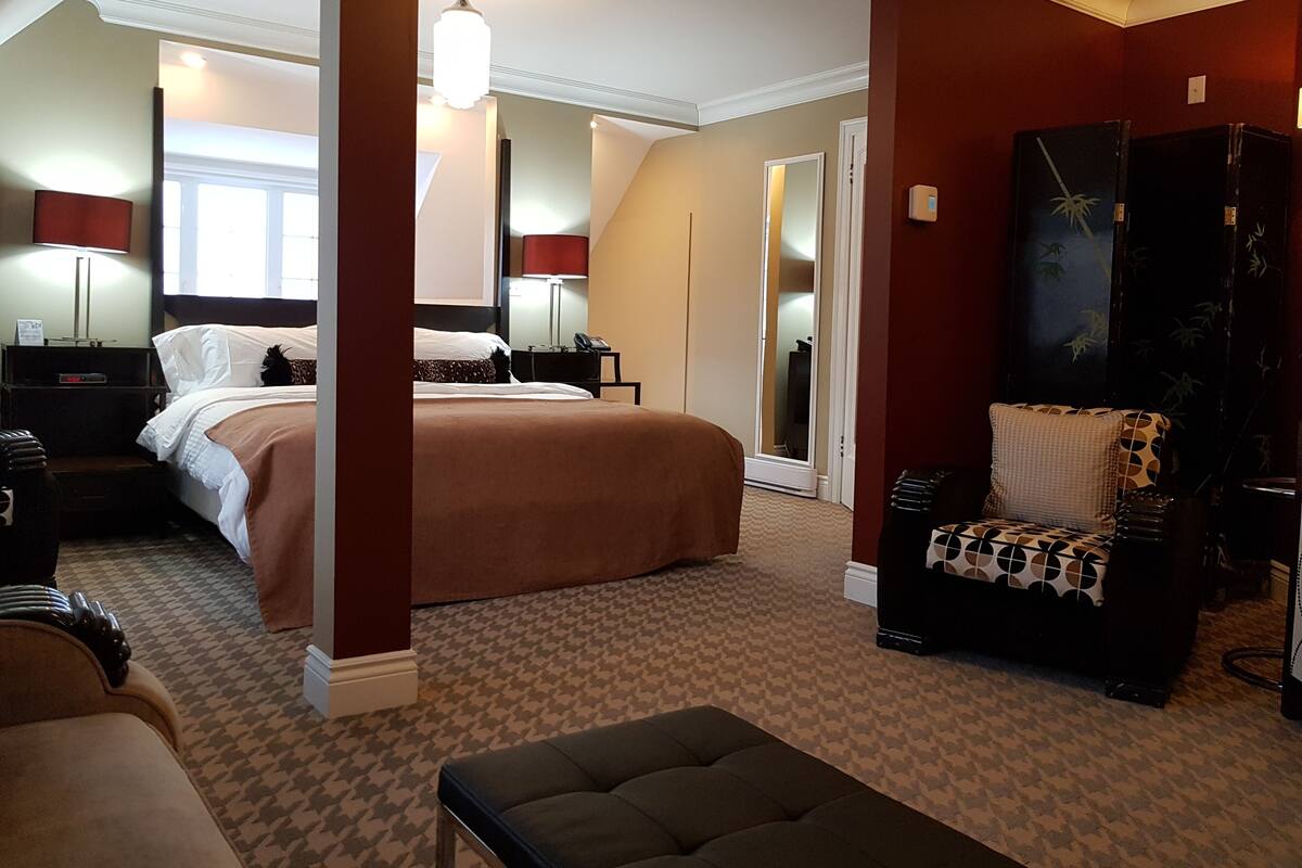 A hotel room with a large bed, a sitting area with a chair, a desk, and a wardrobe.