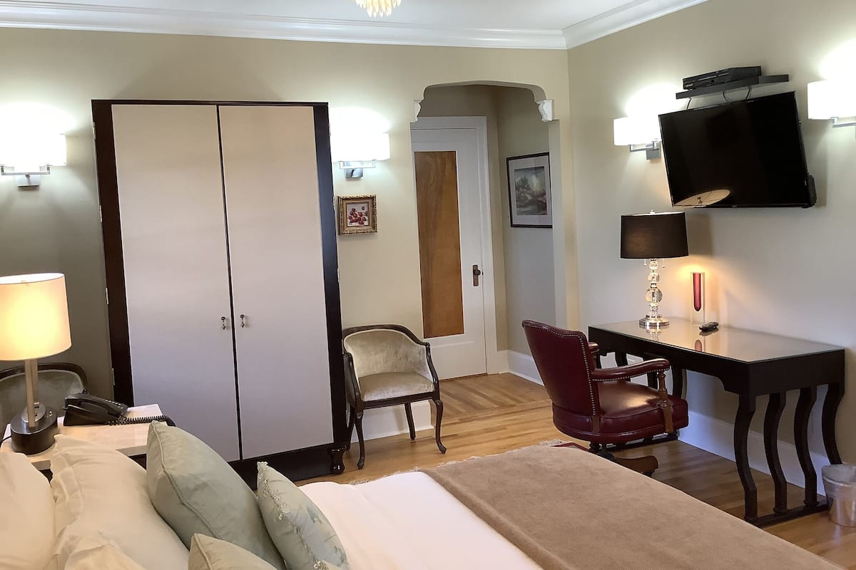 A hotel room with a bed, desk, TV, wardrobe, and a chair.