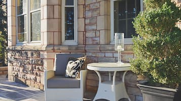 A stone building with a window, a wicker chair with a cushion, and a small table with a glass.
