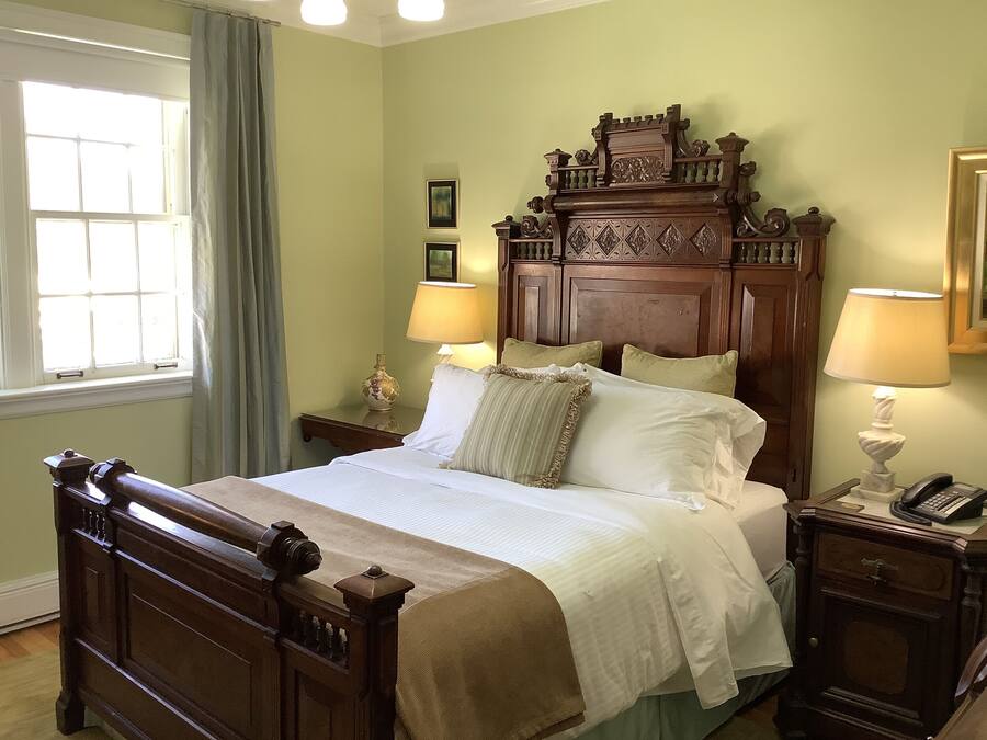 A neatly made bed with a wooden headboard, two bedside tables with lamps, and a window with curtains.