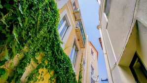 Une rue étroite, bordée de bâtiments des deux côtés, l’un ayant un balcon et l’autre une fenêtre.