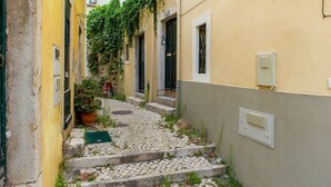 Une ruelle étroite pavée de pierres, avec des marches menant à un immeuble à la façade jaune et à la porte verte.