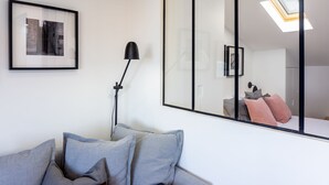 A modern room with a grey sofa, a floor lamp, and a large mirror reflecting a bed with pillows. - Turquoise River View II by LovelyStay (Lisboa)