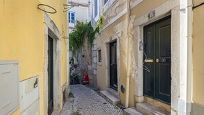 A narrow cobblestone street between buildings with yellow and beige facades, a black door, and a red mailbox. - Traditional Alfama View by LovelyStay (Lisboa)