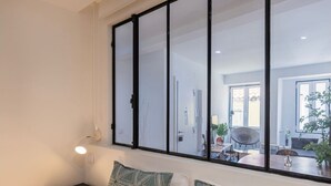 A modern living room with a large window, a sofa, a small table, and a lamp. - Traditional Alfama View by LovelyStay (Lisboa)