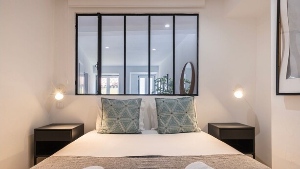 A modern hotel room with a large bed, two patterned pillows, a view of the outdoors through a window, and a neatly made bed with towels. - Traditional Alfama View by LovelyStay (Lisboa)