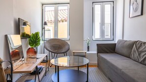 A modern living room with a sofa, a round glass table, a wicker chair, a small side table, and a potted plant. - Traditional Alfama View by LovelyStay (Lisboa)