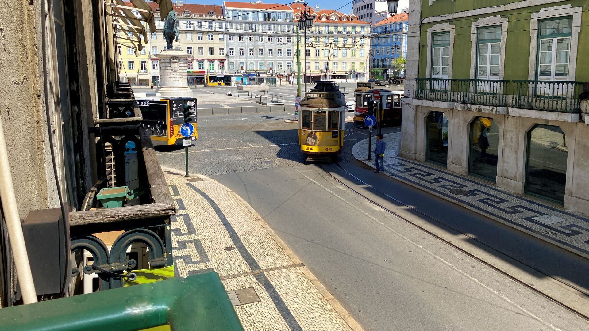 A tram on a city street with buildings and a statue in the background.