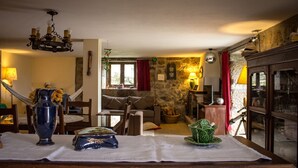 Een gezellige woonkamer met een stenen muur, een open haard, een eettafel met een vaas en een decoratieve schaal, en een kroonluchter.