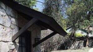 Ein Steinhaus mit überdachter Terrasse, auf der sich ein Tisch, Stühle, ein Blumentopf und eine Steinmauer befinden.