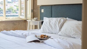 A hotel room with a bed, a small table with a cup and saucer, and a window with a view of buildings. - Blue Oporto Home River Front - Ribeira (Vila Nova de Gaia)