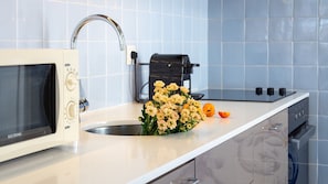 Uma cozinha com micro-ondas, pia, torneira, cafeteira e um arranjo de flores.