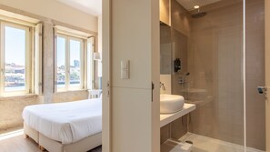 A hotel room with a bed, a bathroom with a shower, and a view of the city. - Blue Oporto Home River Front - Ribeira (Vila Nova de Gaia)