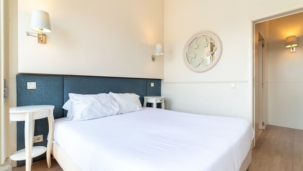A hotel room with a large bed, two bedside tables, a round mirror, and wall-mounted lamps.