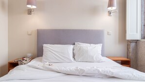 Un lit bien fait, avec une literie blanche, deux tables de chevet et des lampes fixées au mur.