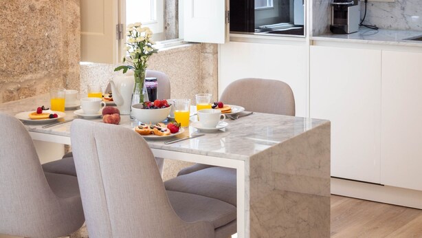 Une table en marbre, des chaises grises à revêtement en tissu et un coin cuisine avec des meubles blancs et un téléviseur composent l’ensemble pour le petit-déjeuner.