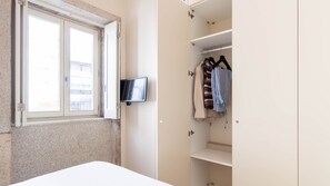 A bedroom with a bed, a window, and a wardrobe with clothes hanging inside.