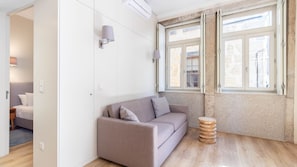 Un salón moderno con un sofá, un taburete de madera y una ventana con vistas al exterior.