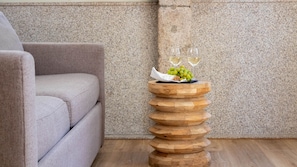 Une petite table d’appoint en bois, sur laquelle se trouve une pile d’assiettes, un verre de vin blanc et une grappe de raisins verts.