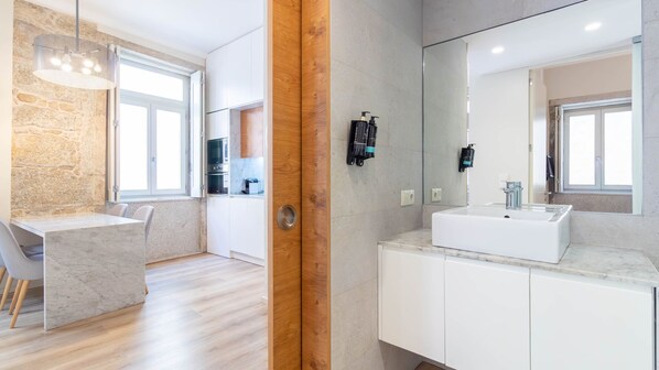 A modern bathroom with a large mirror, a white sink, and a wooden door. - Silver Oporto Home River Front - Ribeira (Vila Nova de Gaia)