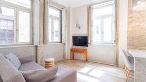 Una sala de estar con un sofá, un televisor sobre un mueble y una pared de piedra.