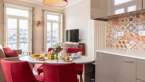 A dining area with a table set for breakfast, red chairs, a TV on the wall, and a city view through large windows.