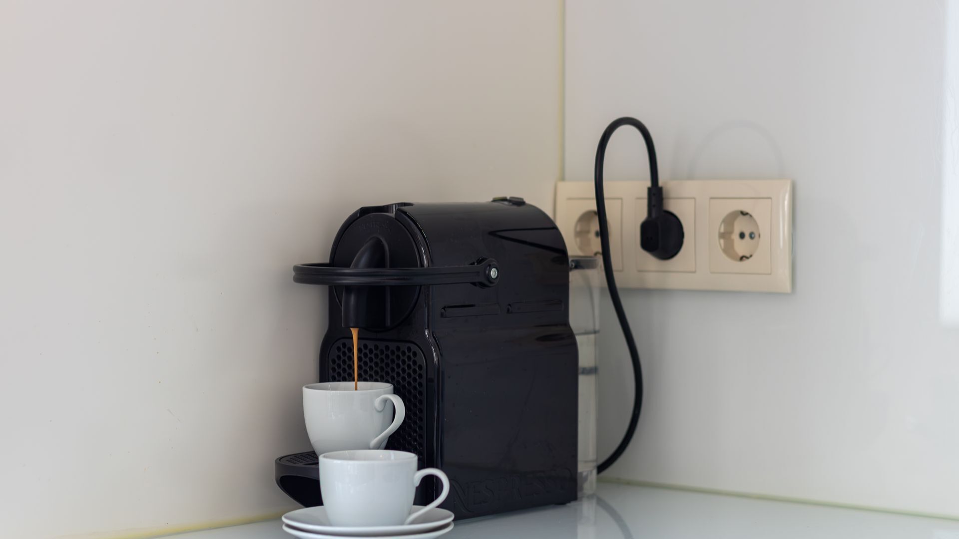 Eine Kaffeemaschine mit Tasse und Untertasse auf einem Tisch, verbunden mit einer Steckdose.