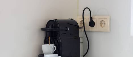 Eine Kaffeemaschine mit Tasse und Untertasse auf einem Tisch, verbunden mit einer Steckdose.