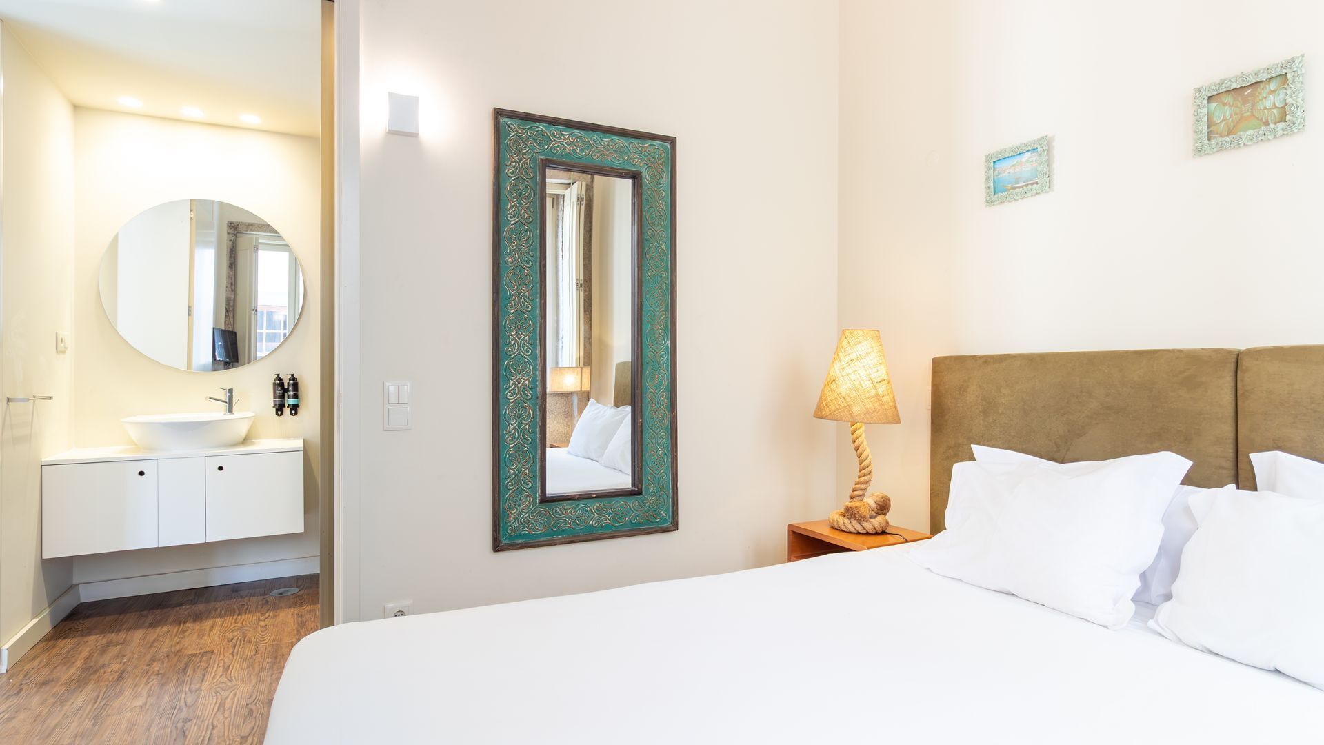 A hotel room with a bed, a bedside lamp, a large mirror, a round mirror, a sink, and a cabinet.