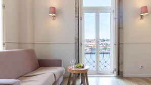 A room with a sofa, a small round table with a fruit bowl and glasses, and a view through a glass door to a body of water. - Purple Oporto Home River Front - Ribeira (Vila Nova de Gaia)