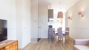 A modern living room with a flat-screen TV, a wooden TV stand, a dining area with a table and chairs, and a kitchen in the background. - Purple Oporto Home River Front - Ribeira (Vila Nova de Gaia)