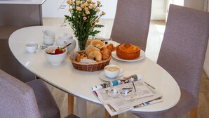 A breakfast setting with a table, a basket of pastries, a vase of flowers, and a newspaper. - Purple Oporto Home River Front - Ribeira (Vila Nova de Gaia)