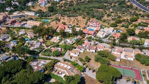 Vista aérea de uma área residencial com casas, espaços verdes e uma quadra de tênis.