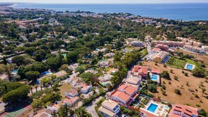 Vista aérea de uma área residencial costeira com vários edifícios, áreas verdes e piscinas.